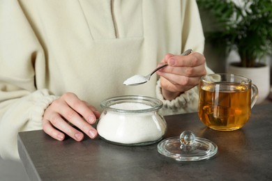 Woman adding sugar into aromatic tea at grey table indoors, closeup