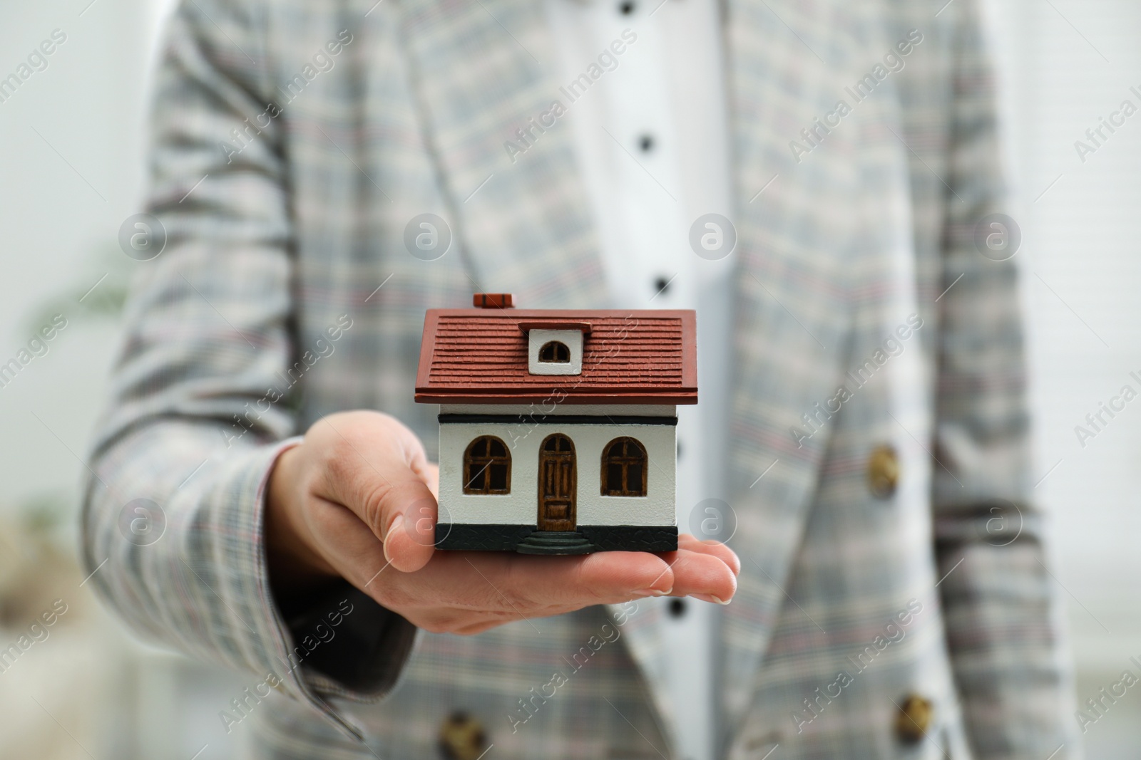 Photo of Real estate agent holding house model indoors, closeup