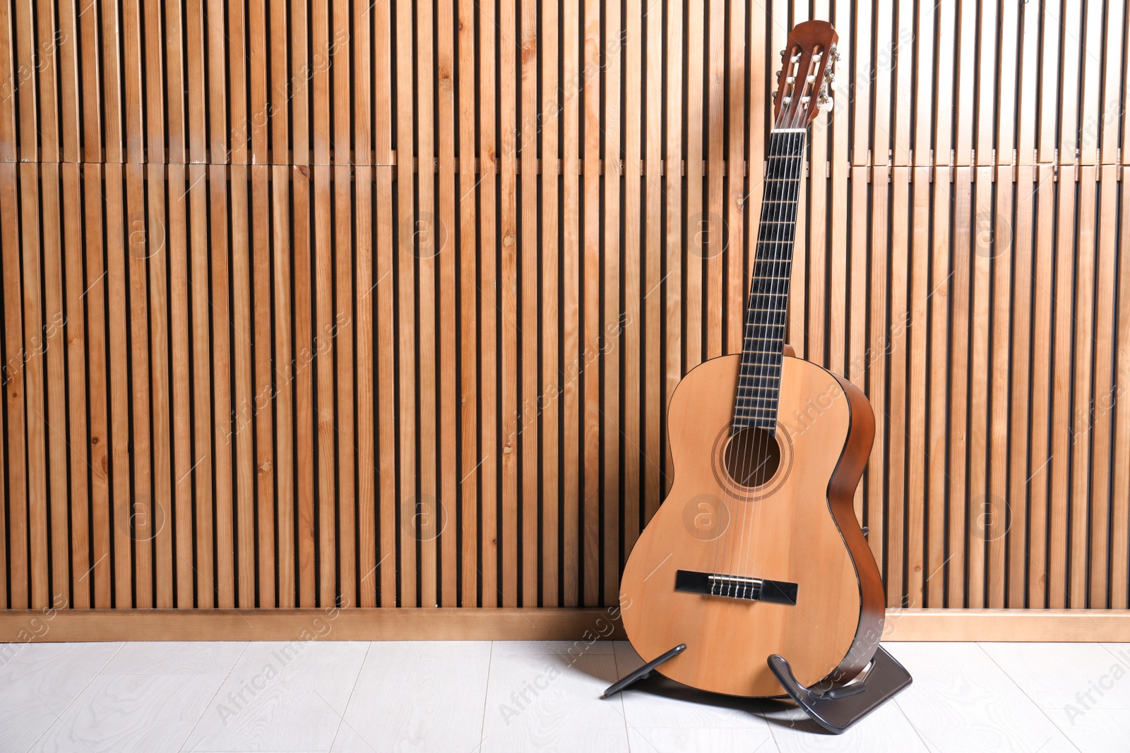 Photo of Stand with classical guitar near wooden wall. Space for text