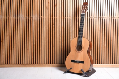 Photo of Stand with classical guitar near wooden wall. Space for text