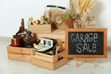 Photo of Sign Garage Sale written on blackboard and many different stuff near white wall