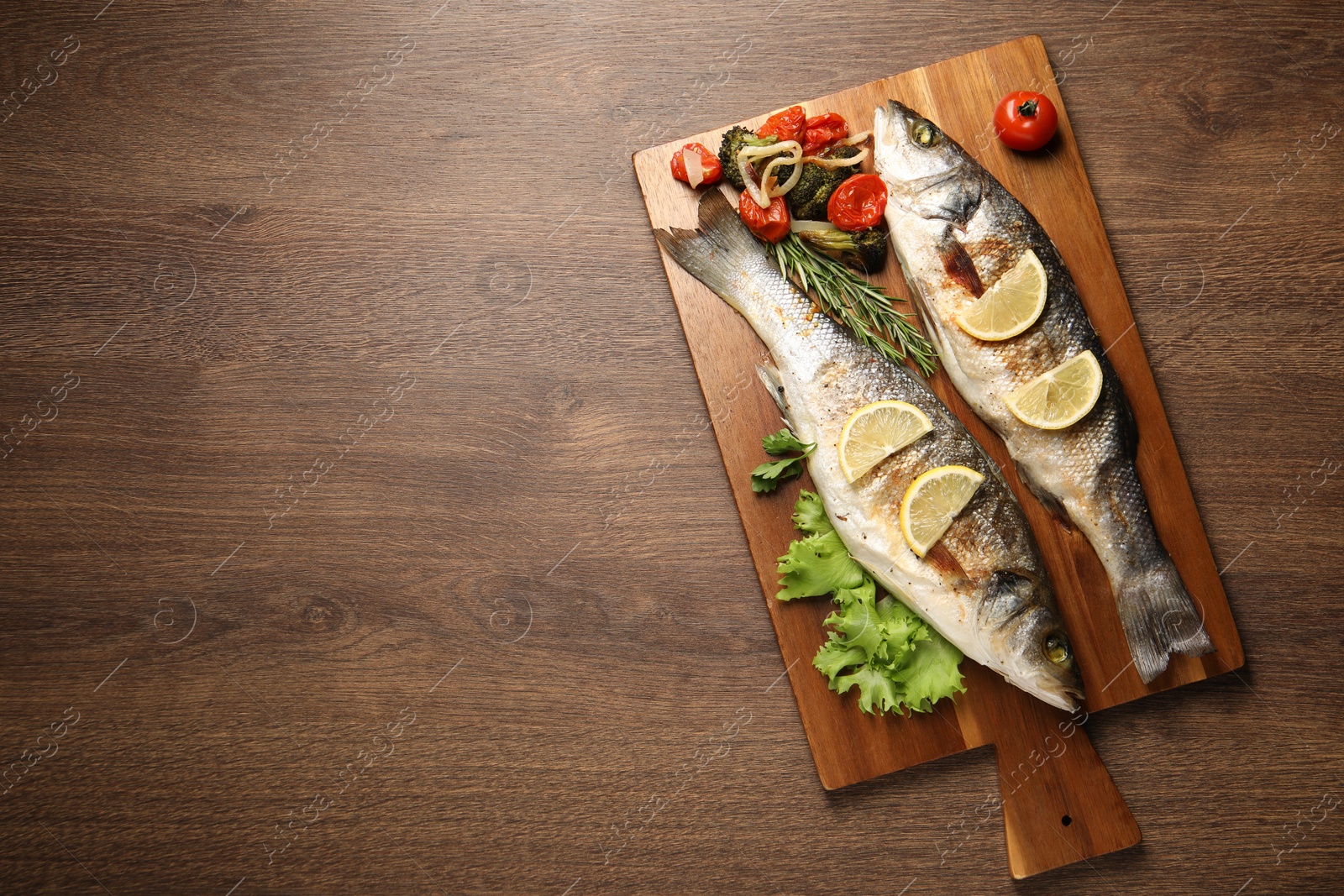 Photo of Delicious baked fish and vegetables on wooden table, top view. Space for text