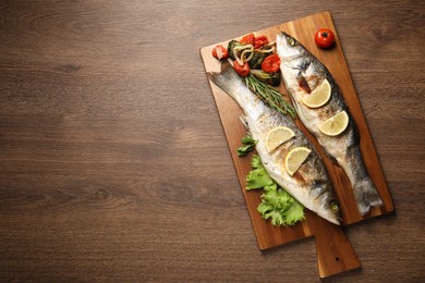 Photo of Delicious baked fish and vegetables on wooden table, top view. Space for text