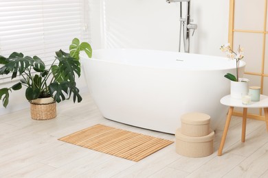 Stylish bathroom interior with bath tub, houseplants and bamboo mat