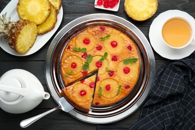 Delicious cut pineapple pie with cherry and tea served on black wooden table, flat lay