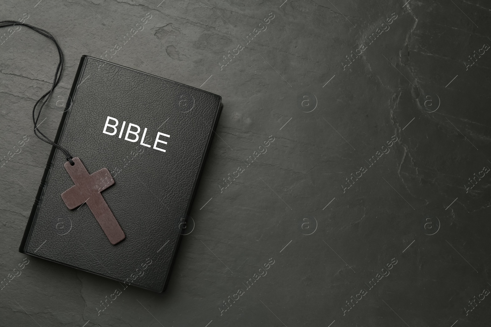 Photo of Christian cross and Bible on black table, top view. Space for text