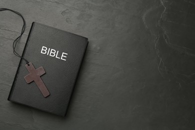 Photo of Christian cross and Bible on black table, top view. Space for text