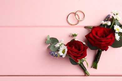 Photo of Stylish boutonnieres and rings on pink wooden table, flat lay. Space for text