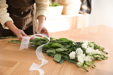 Photo of Florist making beautiful bouquet at table in workshop, closeup