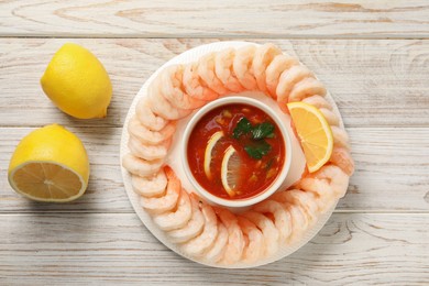 Photo of Tasty boiled shrimps with cocktail sauce and lemon on white wooden table, top view