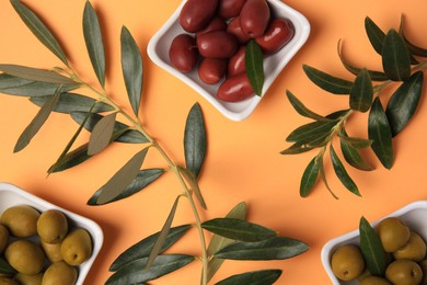 Different fresh olives and green leaves on pale orange background, flat lay