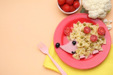 Photo of Creative serving for kids. Plate with cute hedgehog made of delicious pasta, sausages and tomatoes on pale orange table, flat lay. Space for text