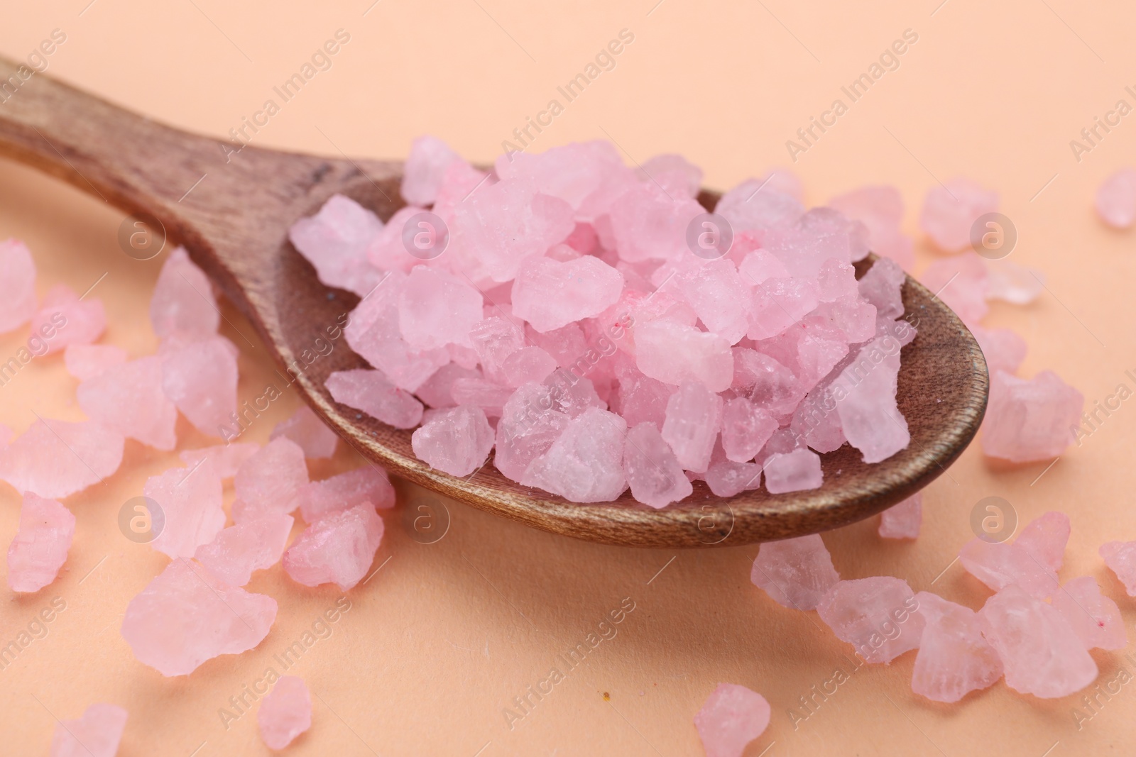 Photo of Spoon with pink sea salt on beige background, closeup