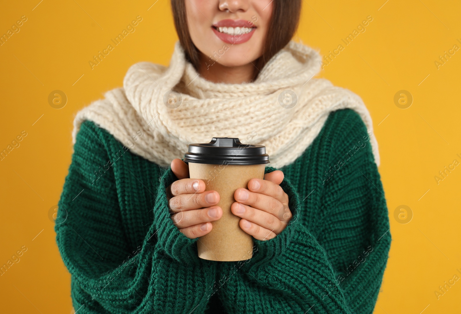 Photo of Happy beautiful woman with paper cup of mulled wine on yellow background, closeup