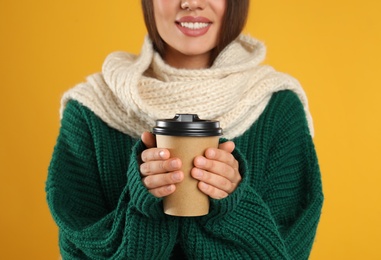 Happy beautiful woman with paper cup of mulled wine on yellow background, closeup