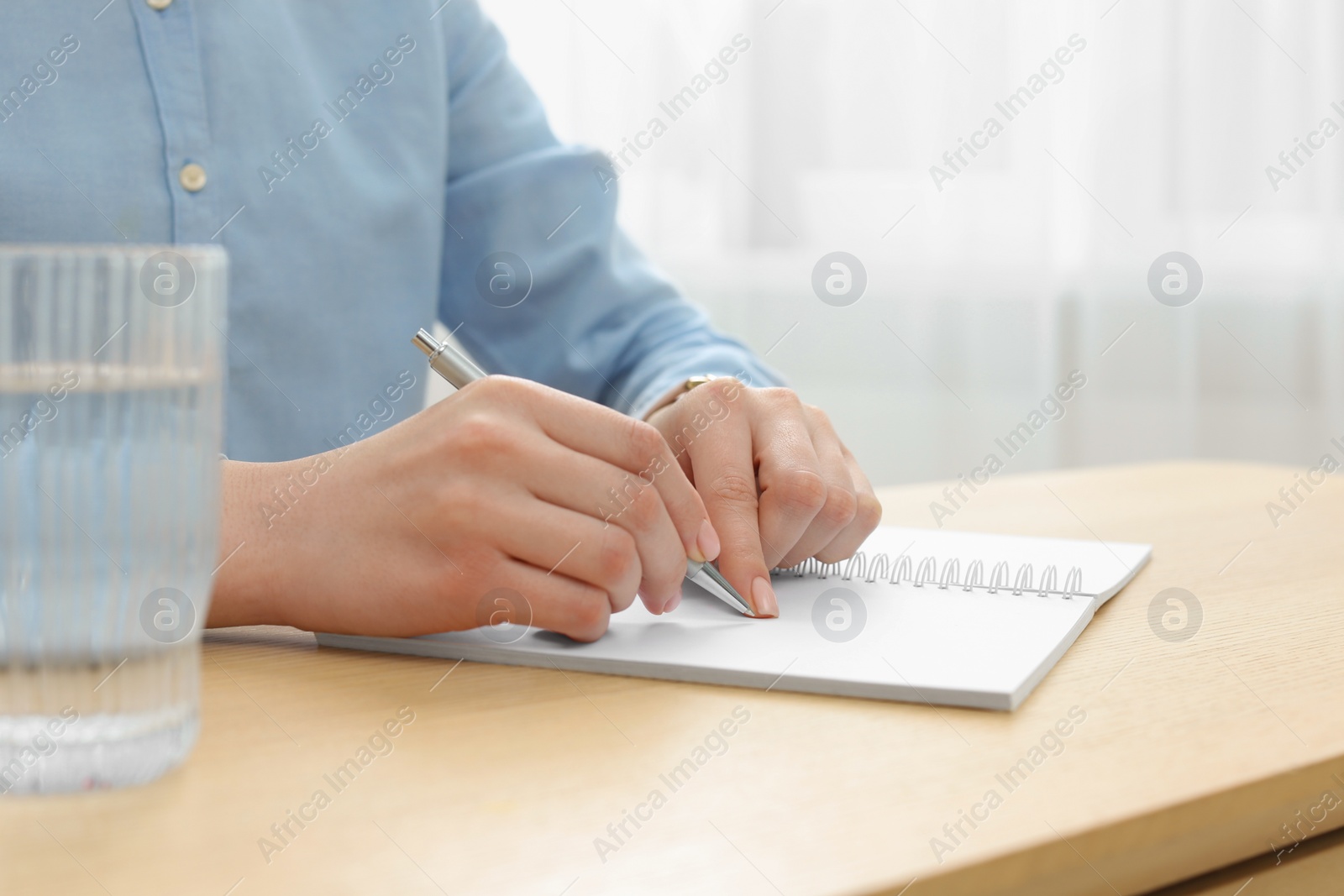 Photo of Woman writing in notebook at wooden table, closeup