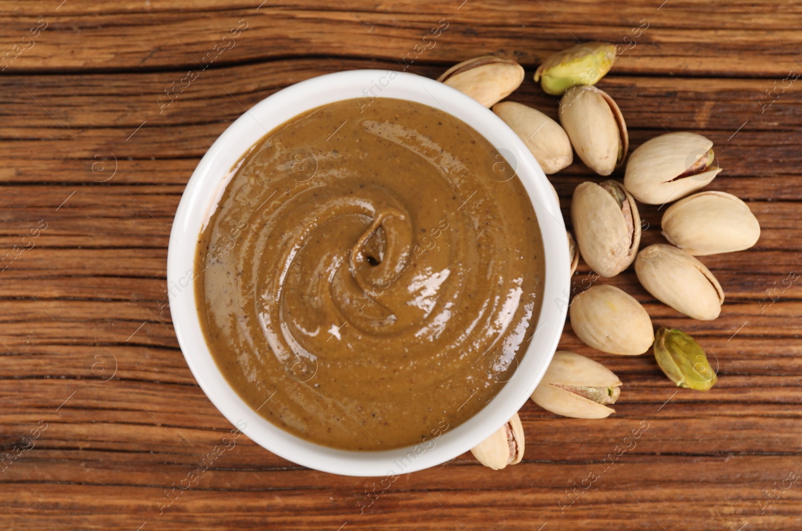 Photo of Delicious nut butter in bowl and pistachios on wooden table, top view