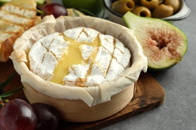 Photo of Tasty baked brie cheese and products on grey table, closeup