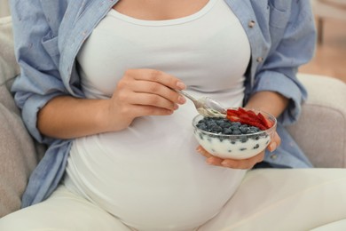 Photo of Pregnant woman eating yogurt with berries at home, closeup. Healthy diet