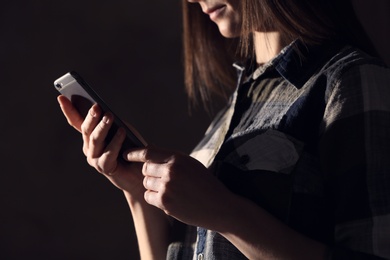Photo of Woman using smartphone against dark background, closeup. Loneliness concept