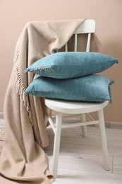 Photo of Soft pillows and warm blanket on chair indoors