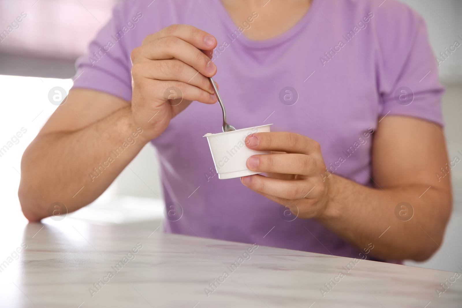 Photo of Young man with tasty yogurt at white marble table, closeup