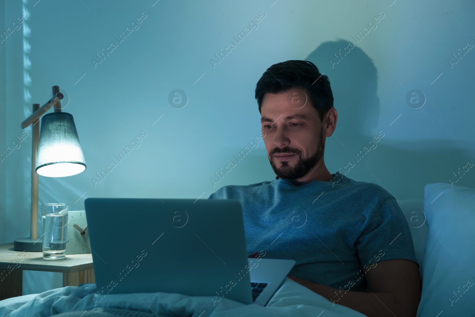 Photo of Man using laptop in bed at night. Internet addiction