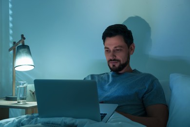 Photo of Man using laptop in bed at night. Internet addiction