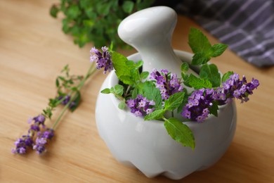 Photo of Mortar with fresh lavender flowers, mint and pestle on wooden table, closeup