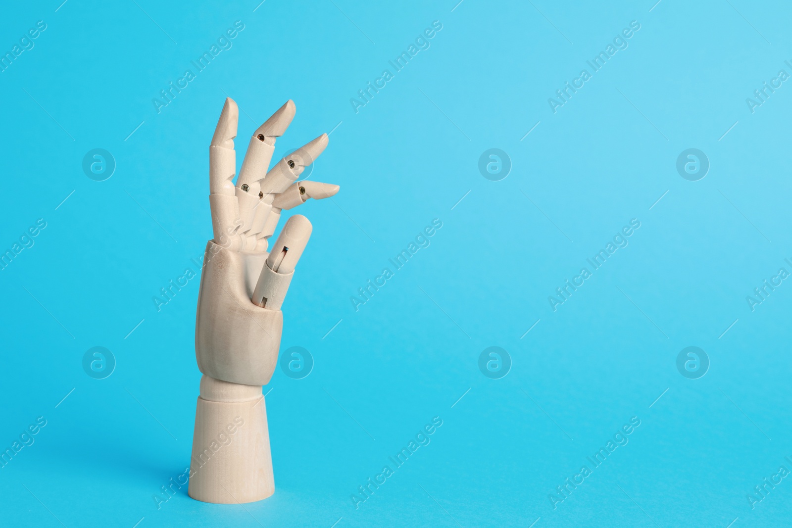 Photo of Wooden mannequin hand on light blue background. Space for text