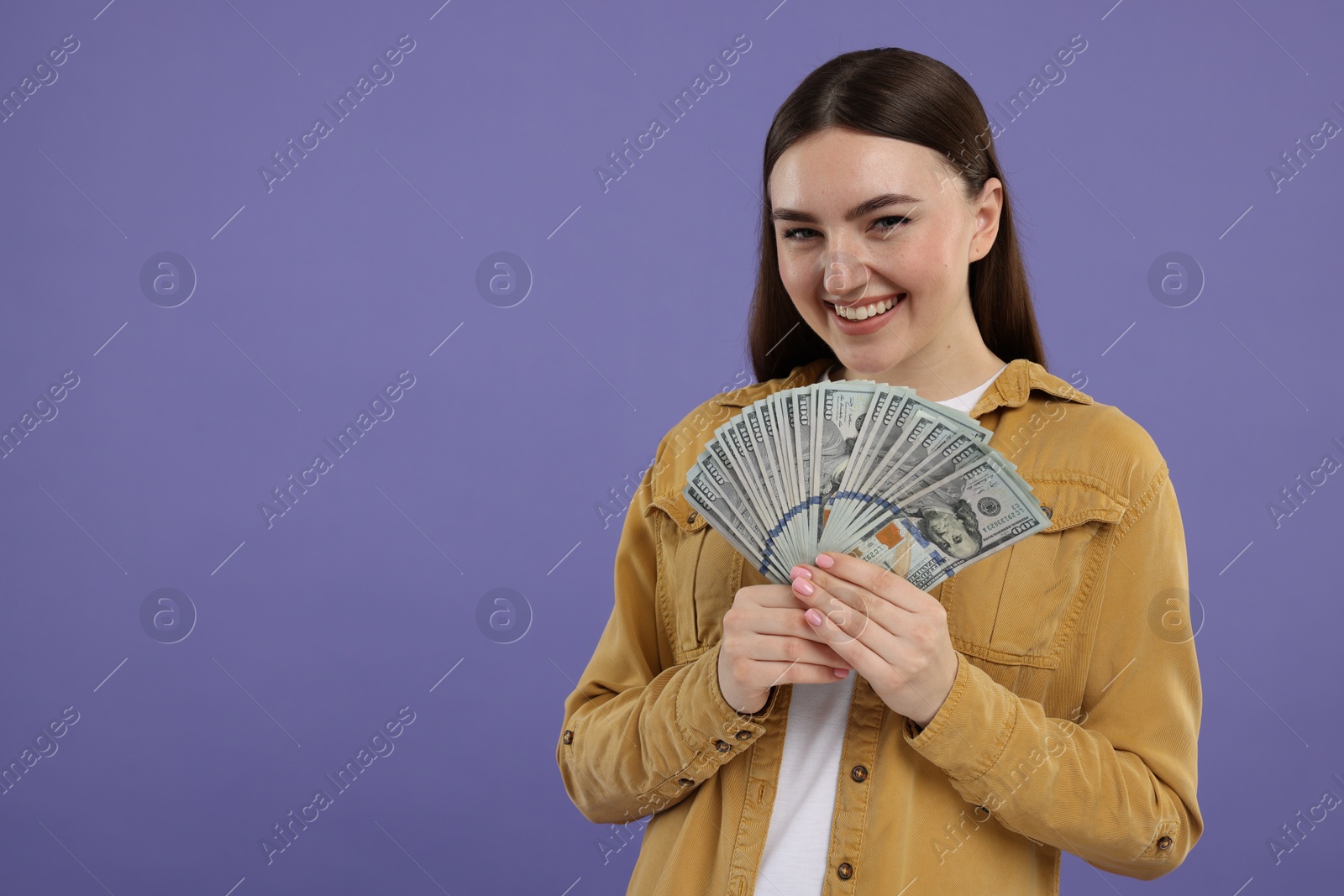 Photo of Happy woman with dollar banknotes on purple background, space for text