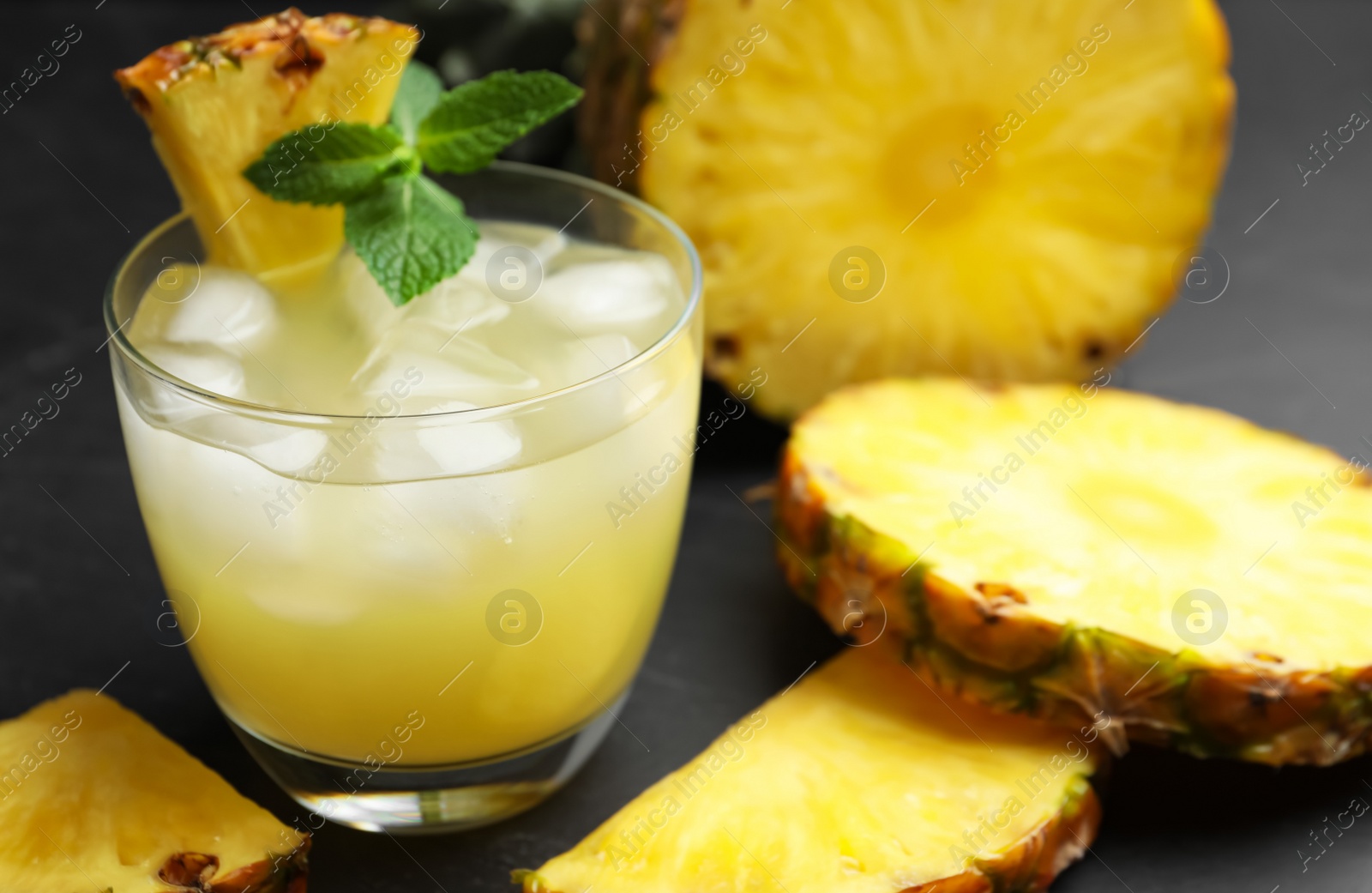 Photo of Delicious fresh pineapple juice with mint and ice cubes on black table, closeup