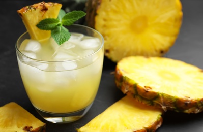 Photo of Delicious fresh pineapple juice with mint and ice cubes on black table, closeup