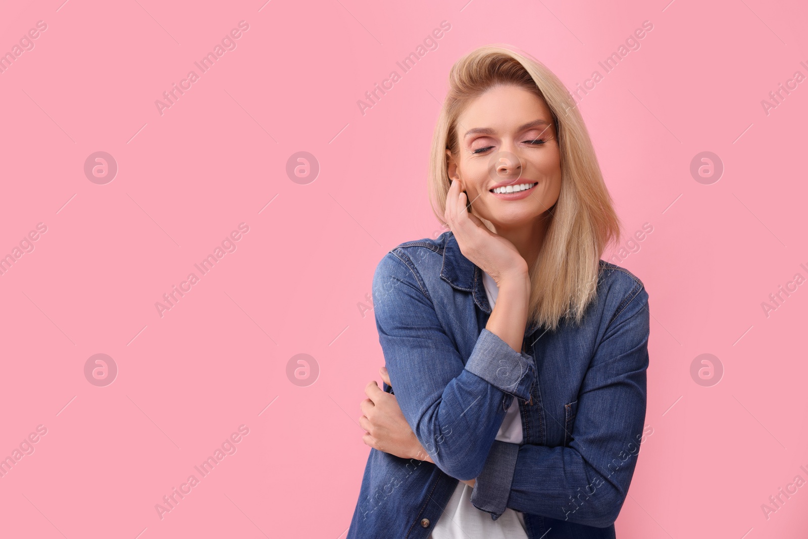 Photo of Portrait of smiling middle aged woman with blonde hair on pink background. Space for text