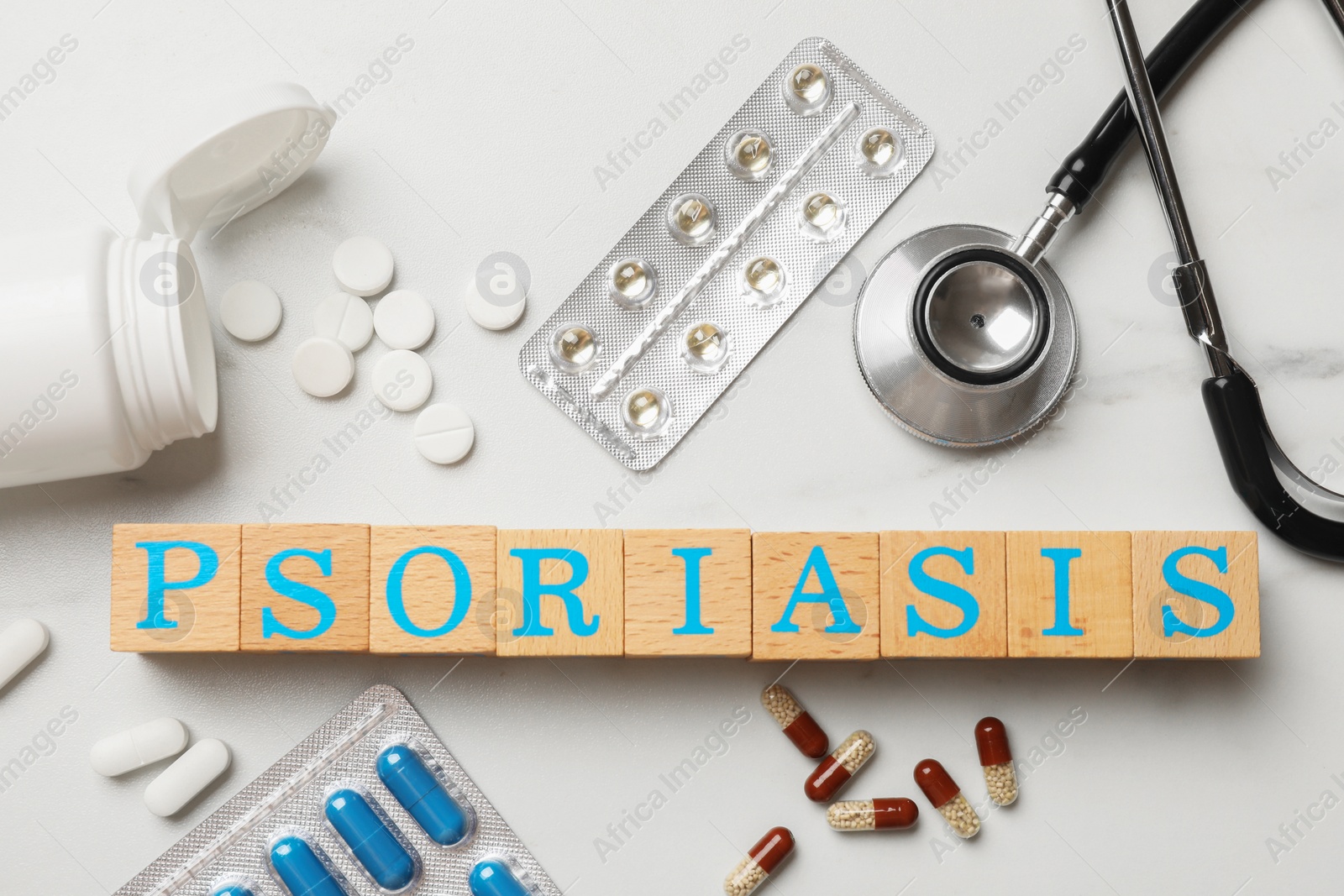 Photo of Word Psoriasis made of wooden cubes with letters, stethoscope and pills on white table, flat lay