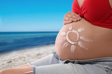 Image of Young pregnant woman with sun protection cream on beach, closeup