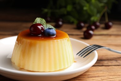Plate of delicious caramel pudding with blueberry, cherry and mint served on wooden table, closeup