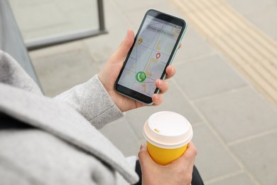 Photo of Woman with cup of coffee ordering taxi on her smartphone outdoors, closeup
