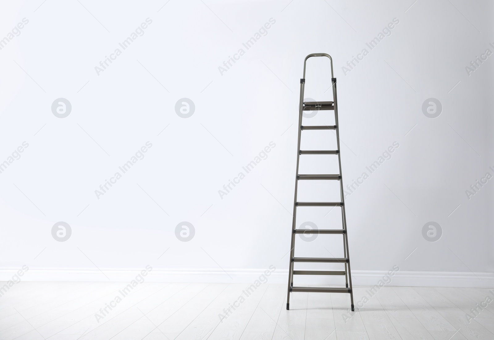 Photo of Modern metal stepladder near white wall. Space for text