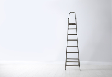 Photo of Modern metal stepladder near white wall. Space for text