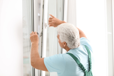 Photo of Mature construction worker repairing plastic window with screwdriver indoors