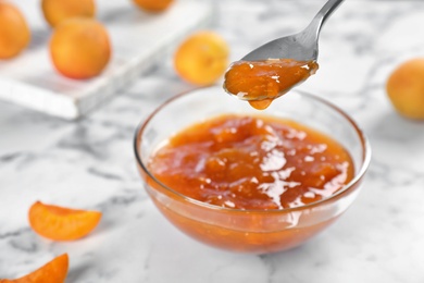 Photo of Bowl and spoon with tasty apricot jam on table