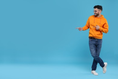 Happy young man pointing at something on light blue background, space for text