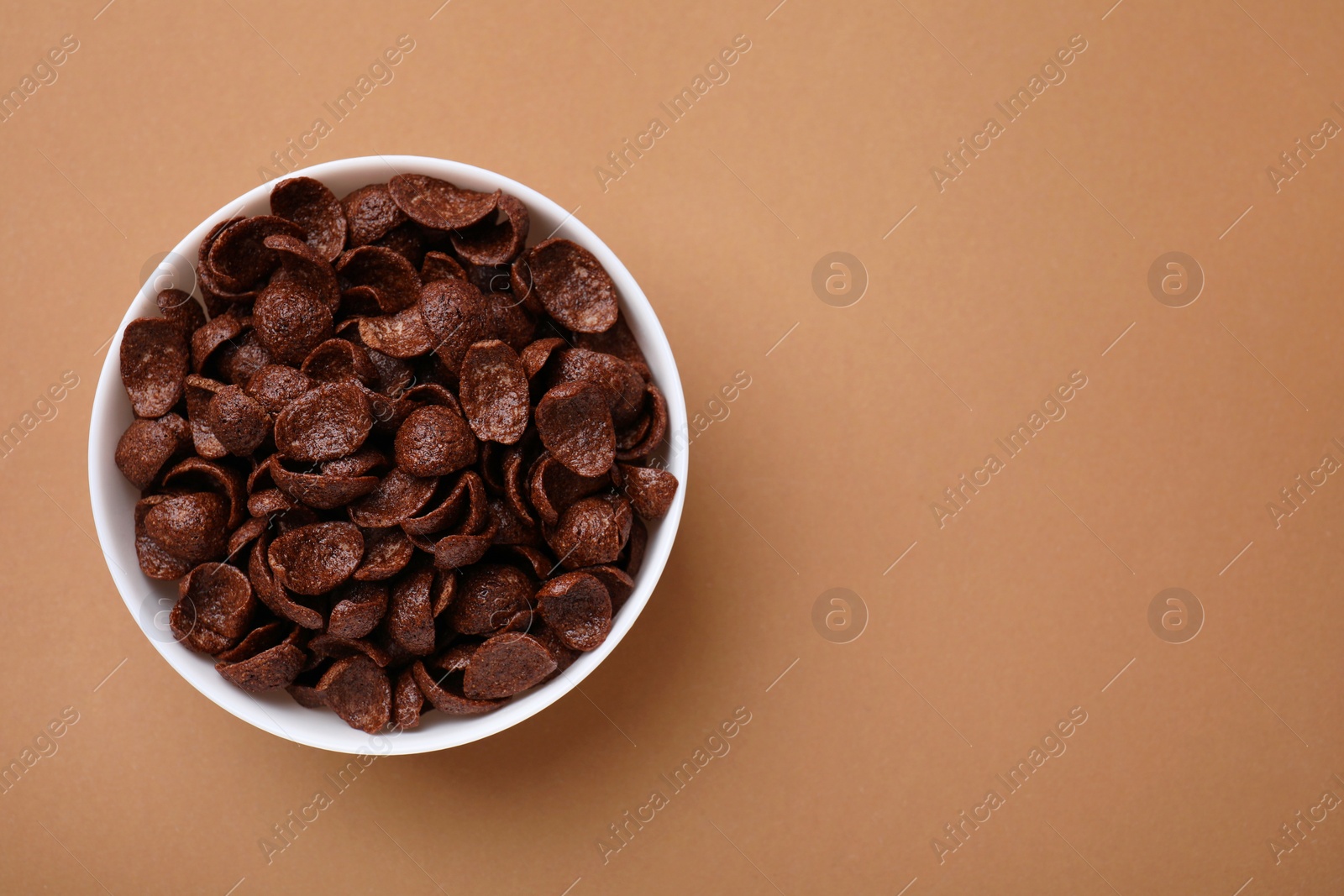 Photo of Breakfast cereal. Chocolate corn flakes in bowl on brown table, top view. Space for text