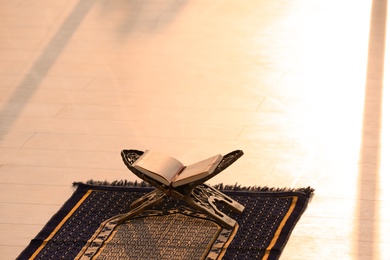 Photo of Rehal with open Quran on Muslim prayer mat indoors. Space for text
