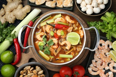 Photo of Saucepan with delicious Tom Yum soup and ingredients on wooden table, flat lay