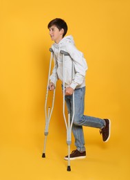 Photo of Teenage boy with injured leg using crutches on yellow background