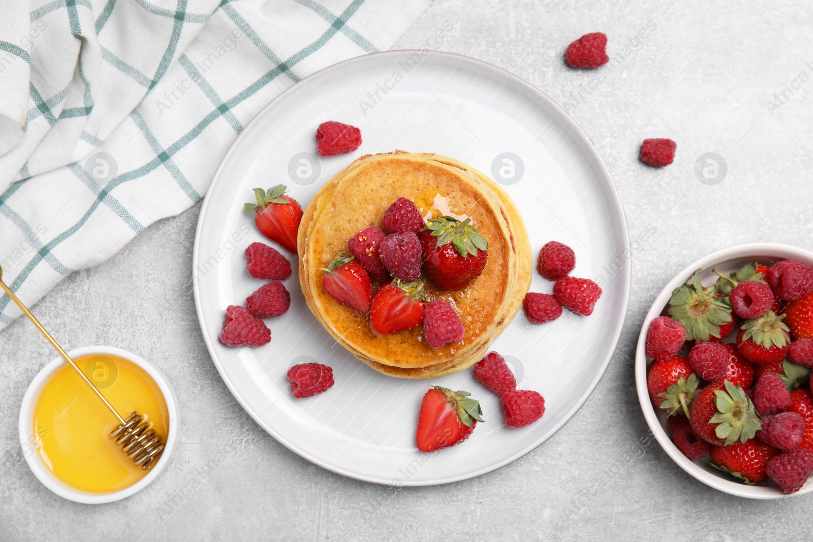 Photo of Tasty pancakes served with honey and berries on light grey table, flat lay