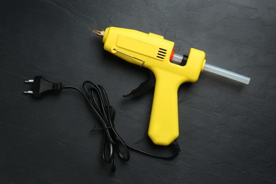 Yellow glue gun with stick on black table, top view