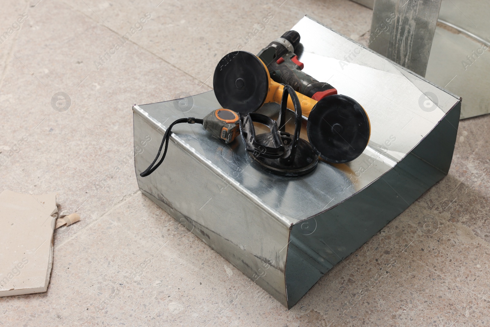 Photo of Yellow suction plate, drill and measuring tape on floor indoors